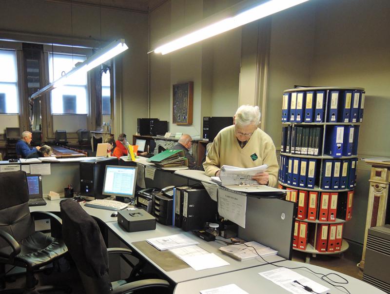 Foto van de binnenkant van het documentatiecentrum in Merksem. Je ziet een toog met computers. En verschillende mensen die opzoekingen doen.